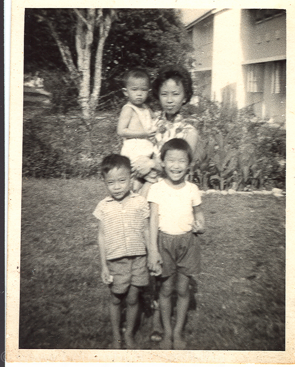 My mum carrying me with my brother Johnny and my sister Janet in the front yard of Wu Lien Teh Gardens, housing quarters for state goverment employees. The picture was probably taken by a neighbor's kid.